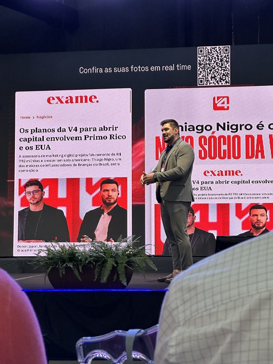 Júnior Kloh no palco, com a matéria da Exame sobre a V4 Company no telão
